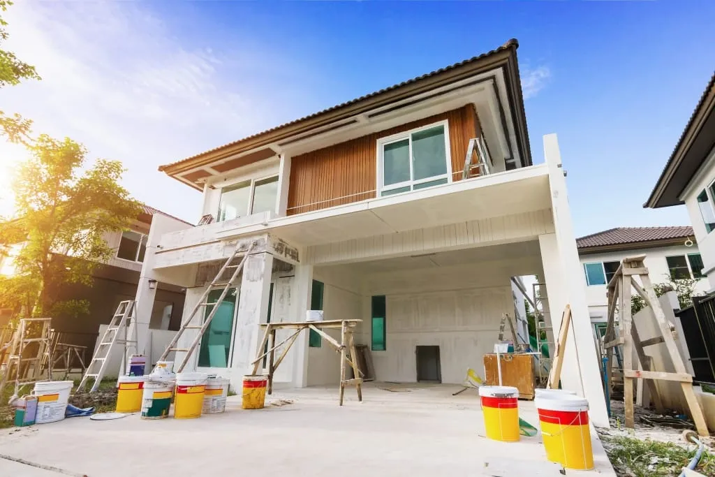 Two-storey house during an exterior repaint, with paint tins in the driveway