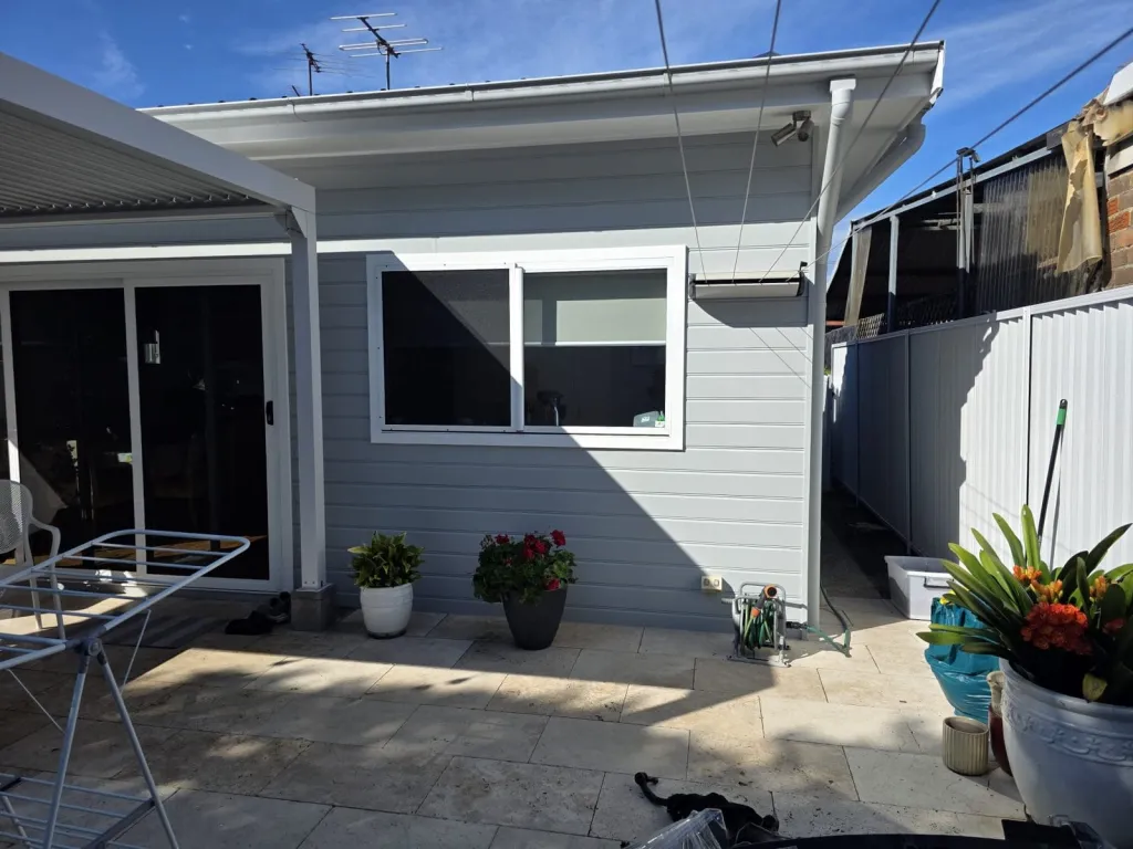 Weatherboard house exterior repainted grey with white trims, gutters and downpipes in a Sydney backyard