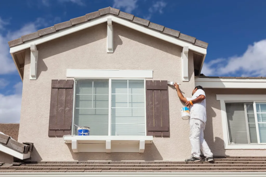 Painter on a ladder painting the rendered exterior of a two-storey house
