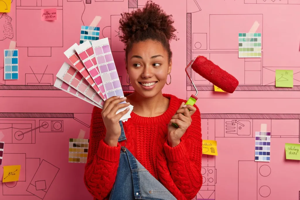 Woman holding colour swatches and a paint roller in front of a pink wall